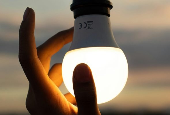 A hand holding a glowing light bulb against a twilight sky, symbolizing ideas and innovation.