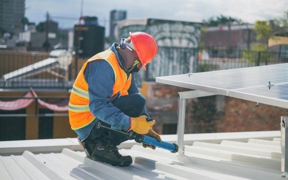 Technician in safety gear installing solar panels on a rooftop, ensuring energy efficiency.
